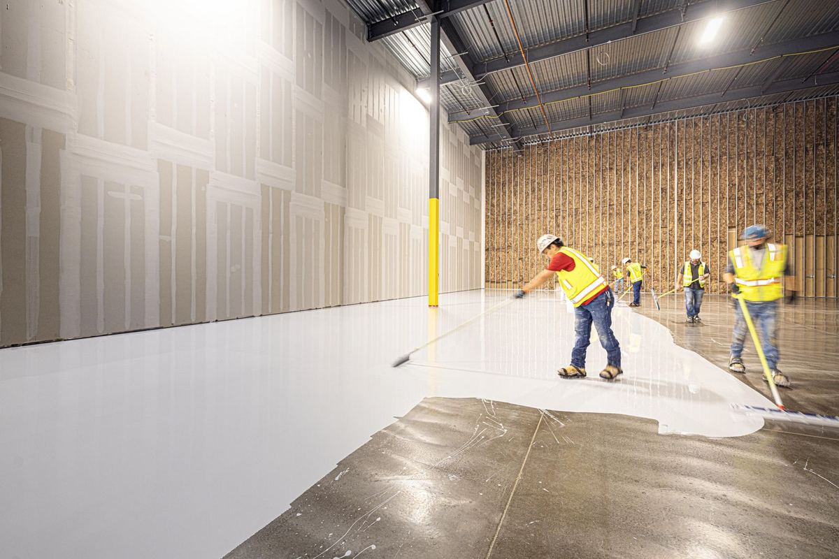 Crew applying a seamless white coating across a large warehouse floor